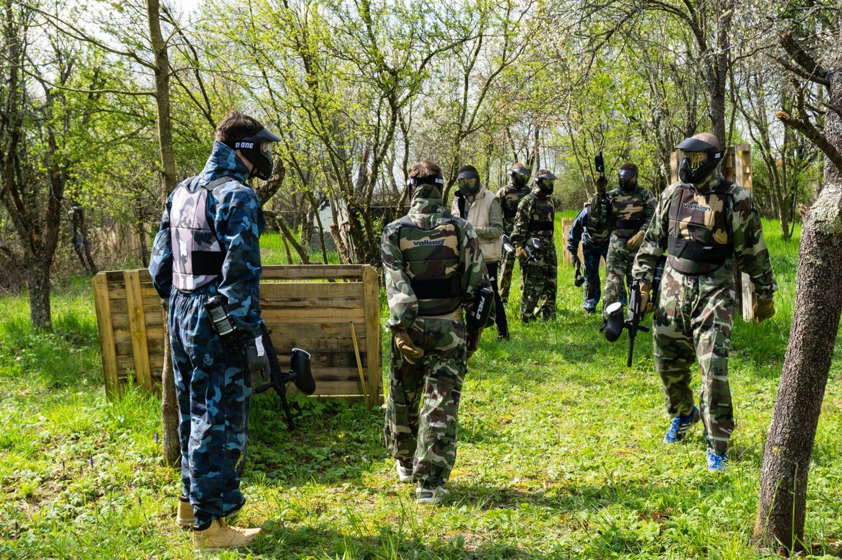 Dvije osobe u maskirnim uniformama igraju paintball iza drvenih zakloništa